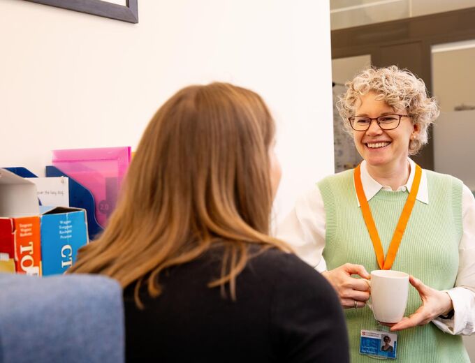Two University staff members chatting and holding hot drinks at the Student Services Centre 